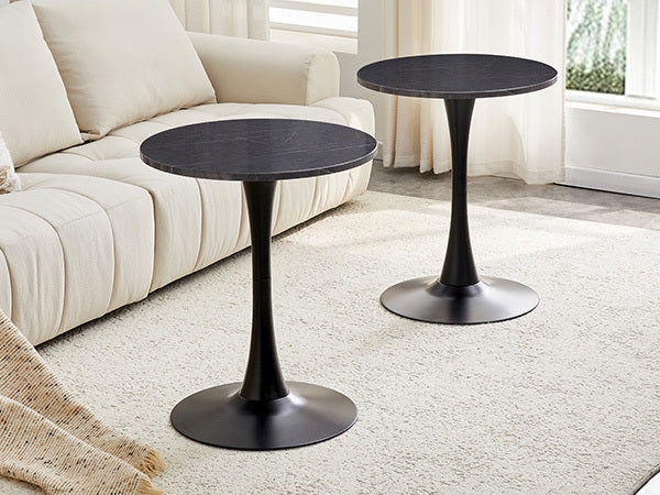 Two black marble-look bistro tables at different heights on a rug beside a cream tufted sofa