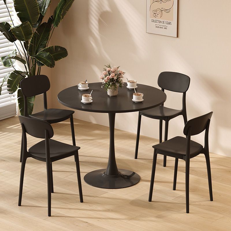 Black round dining table with four black chairs in a bright dining nook with a plant