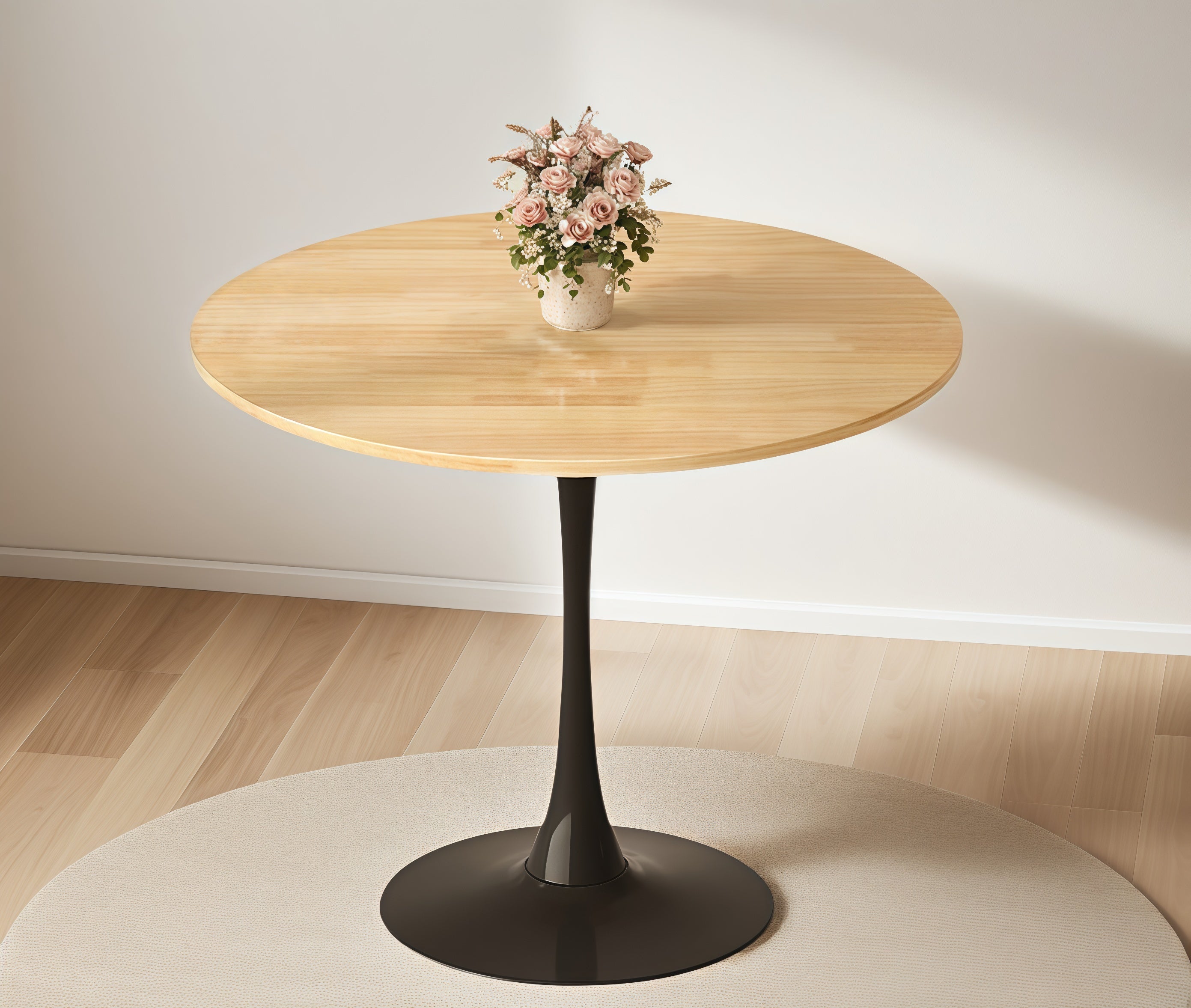 Front view of the natural wood round bistro table with pink flowers on a round rug near a white wall