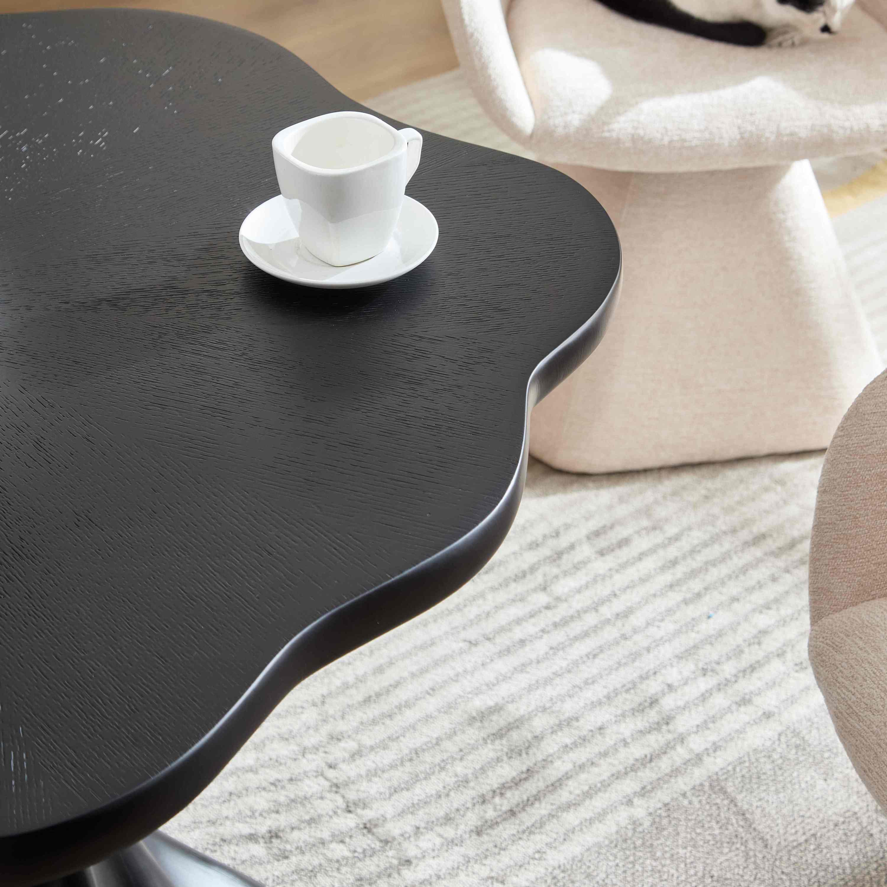 Overhead close-up of the black petal tabletop corner with an espresso cup, boucle chairs around