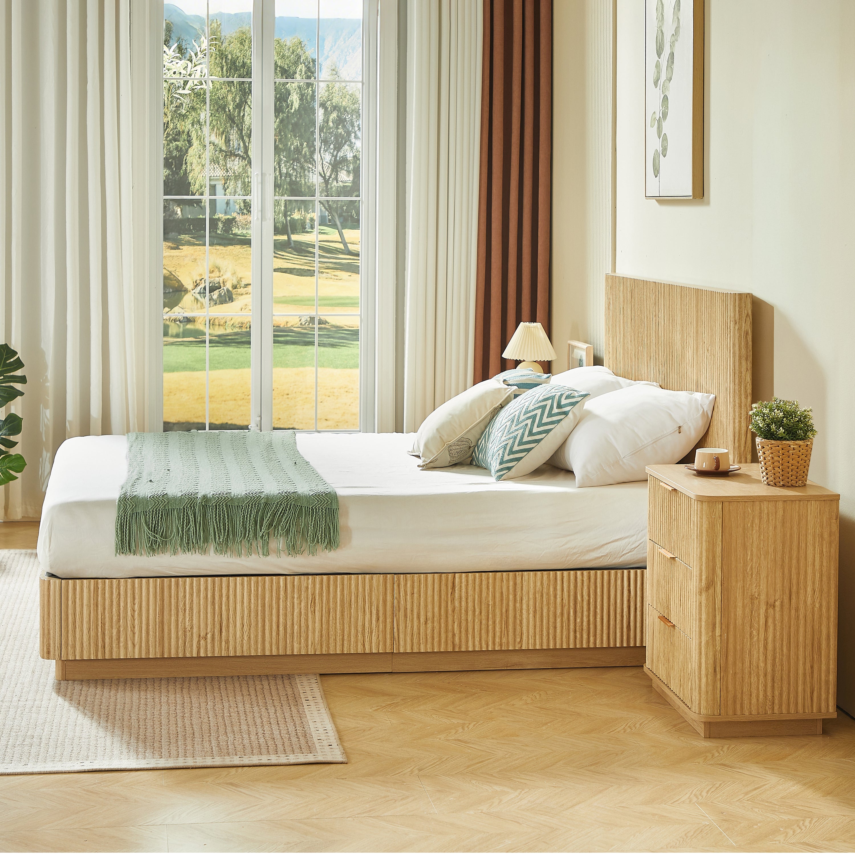 Foot-angle view of light oak fluted queen bed by a window with golf course view and nightstand #Color_Oak