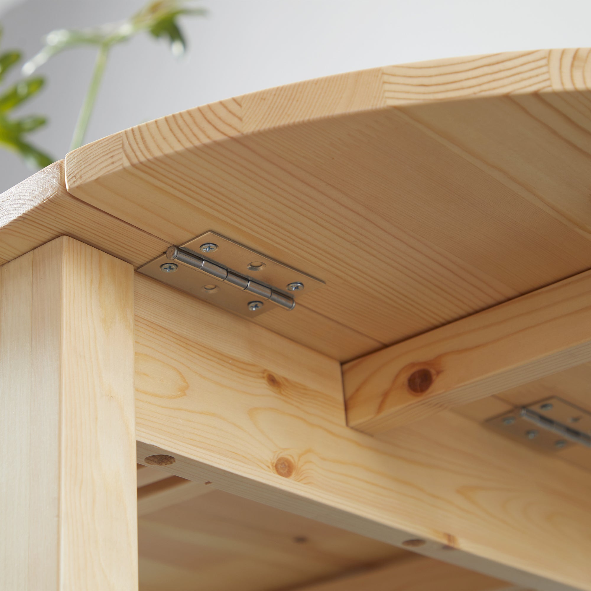 Close-up of the metal drop-leaf hinge screw-mounted under the pine tabletop