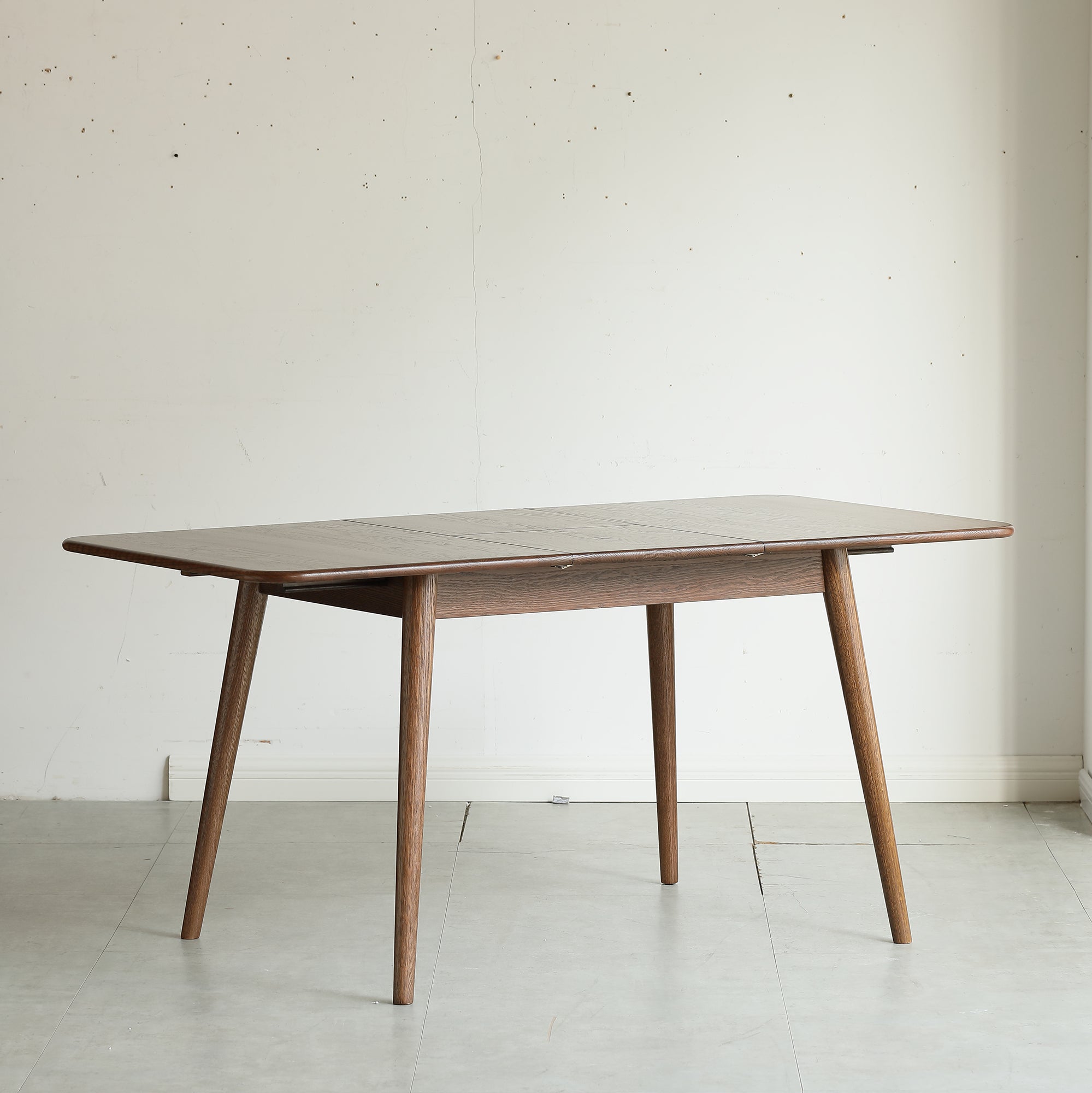 Side view of the walnut oak extendable dining table in a plain studio