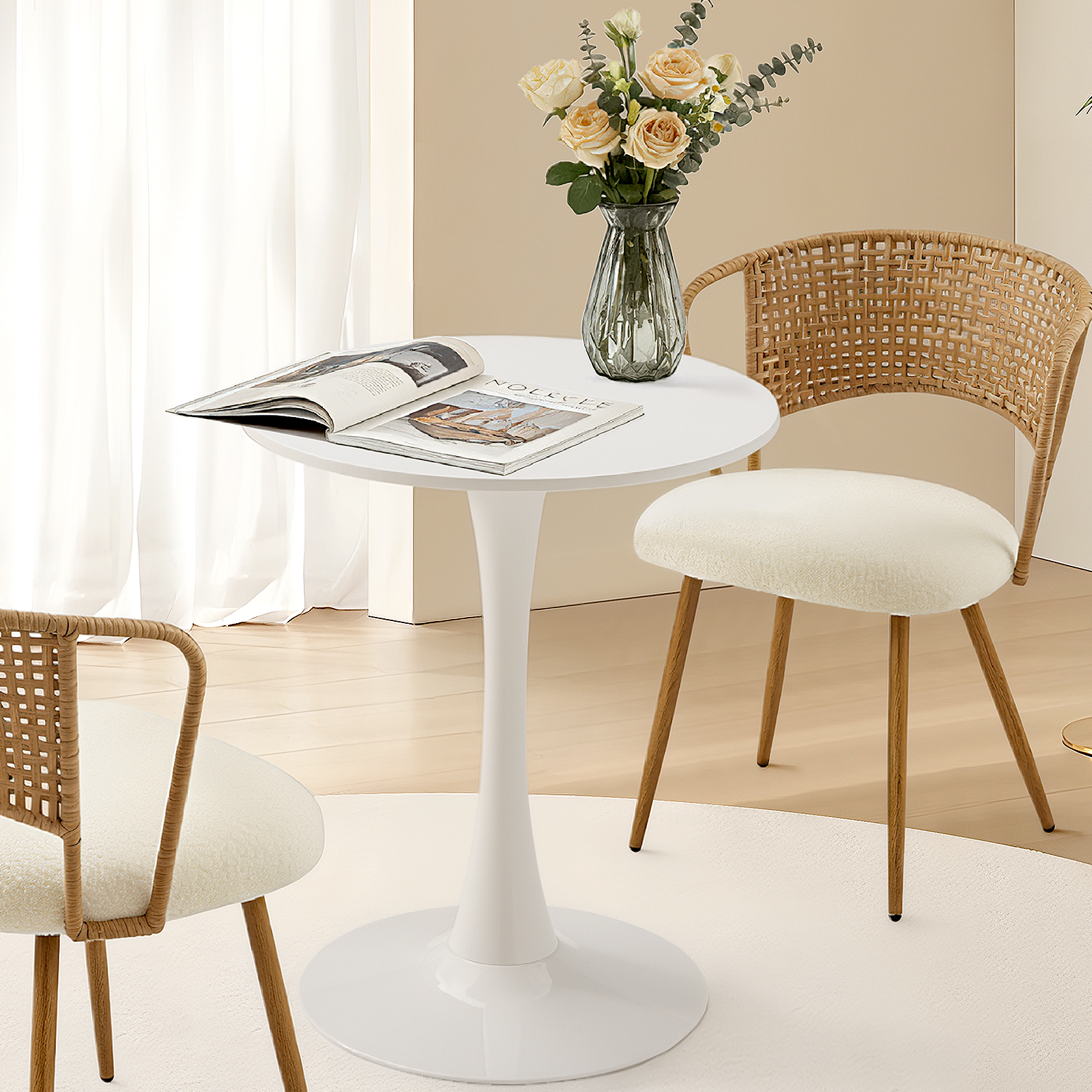 White round tulip bistro table with an open magazine and roses, flanked by rattan chairs