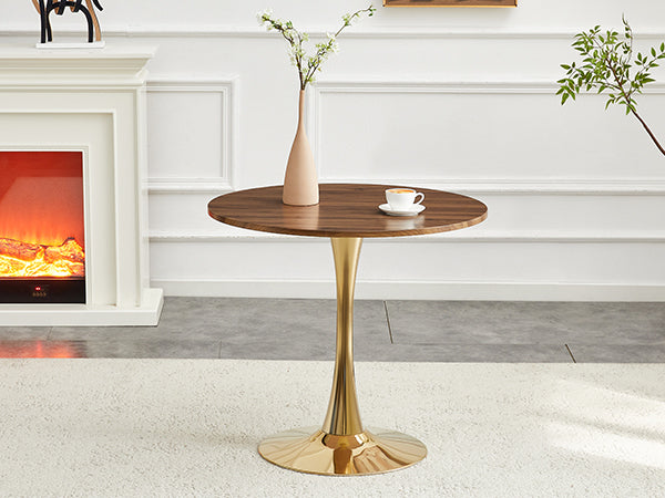 Walnut round dining table with gold pedestal beside a glowing fireplace, three-quarter view
