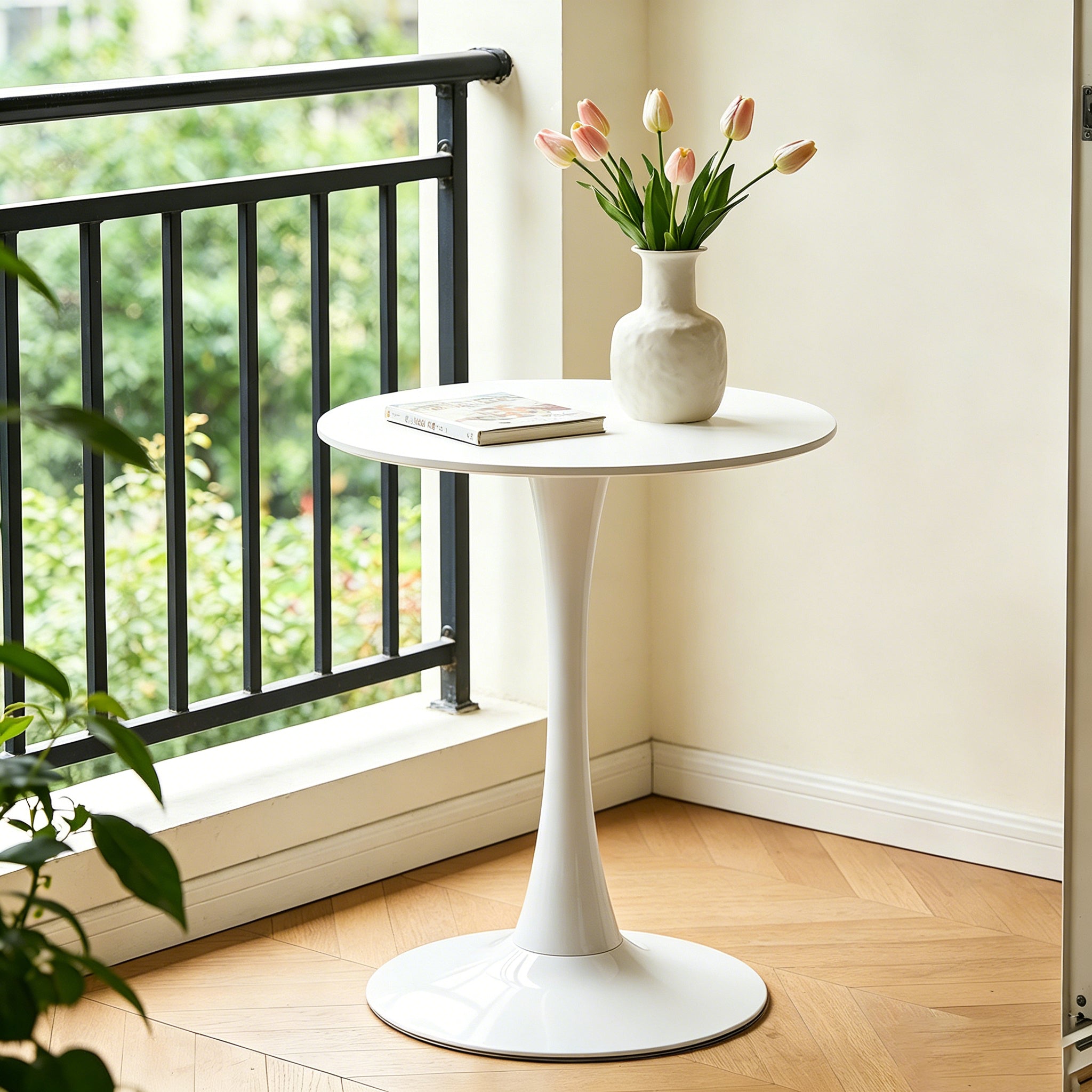 White round tulip bistro table on a balcony corner, styled with tulips and a book by a black railing