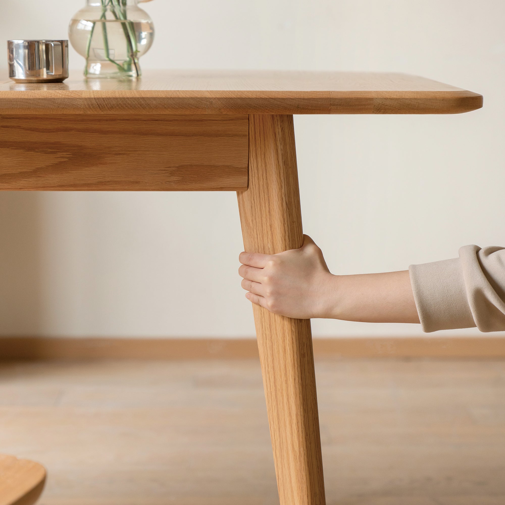 Close-up of a hand gripping the tapered oak table leg below the apron