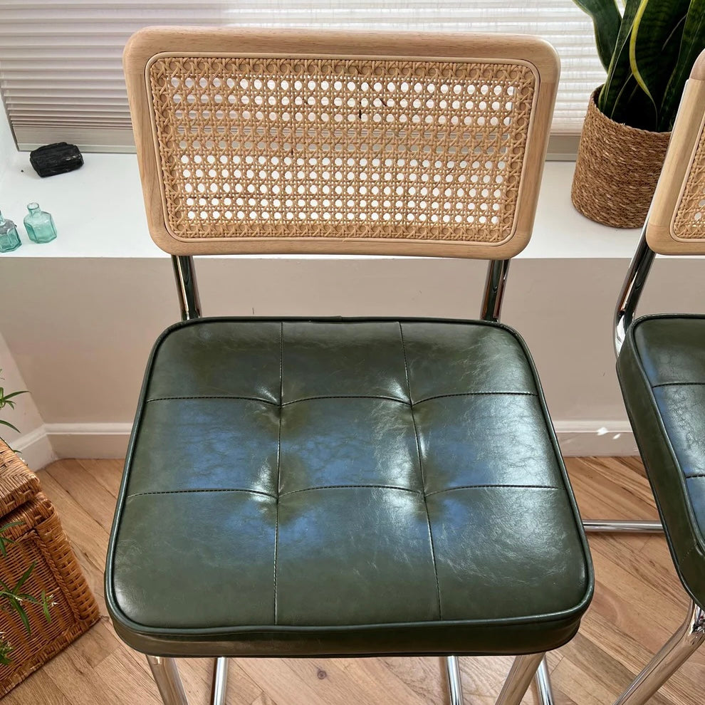 closeup of green vegan leather seat on a mid century modern counter height bar stool with a wood and rattan backrest