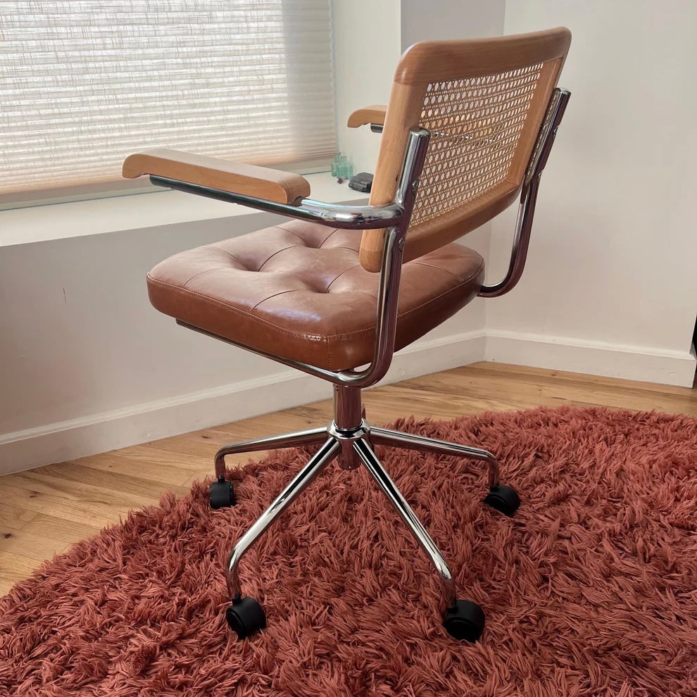 back quarter view of mcm office chair showing stainless steel frame rattan accent on seat back and brown vegan leather seat