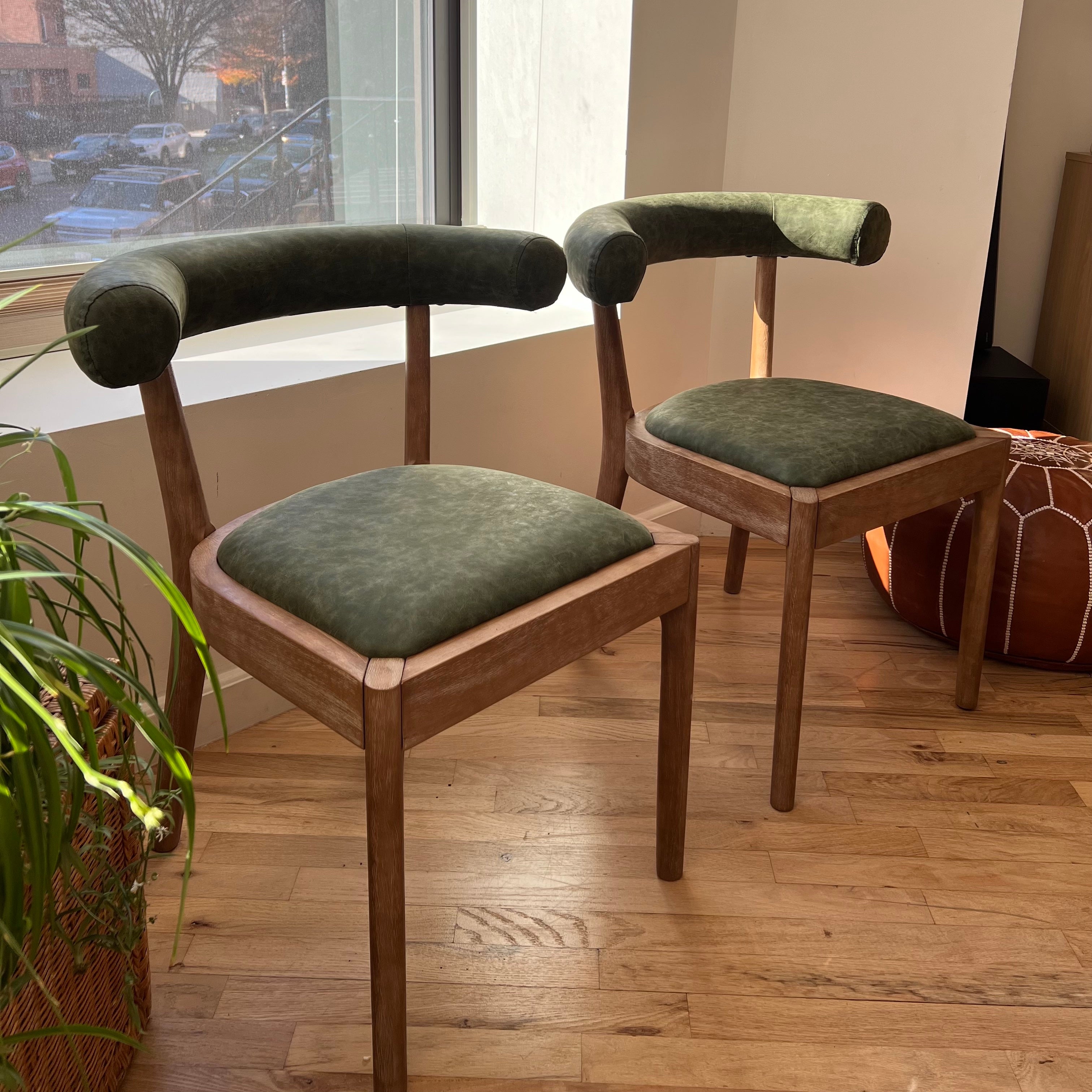 quarter side view of solid wood dining chairs with green vegan leather seats and ergonomic backrests
